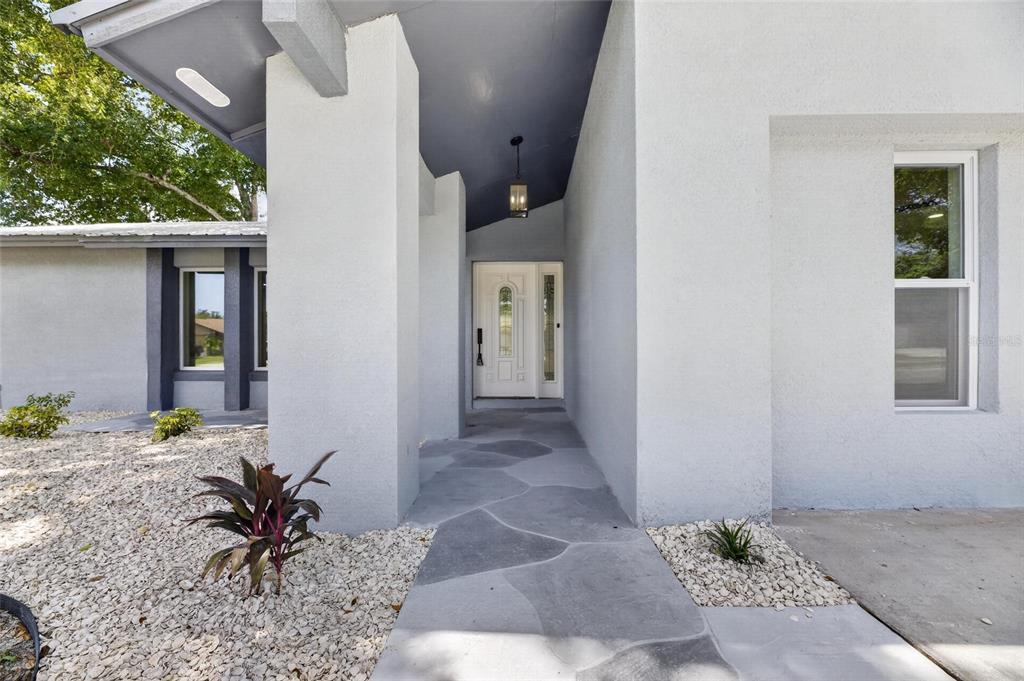A white house exterior features a covered entryway with a stone-patterned walkway and gravel landscaping — 3624 COPPERTREE CIRCLE, BRANDON, FL