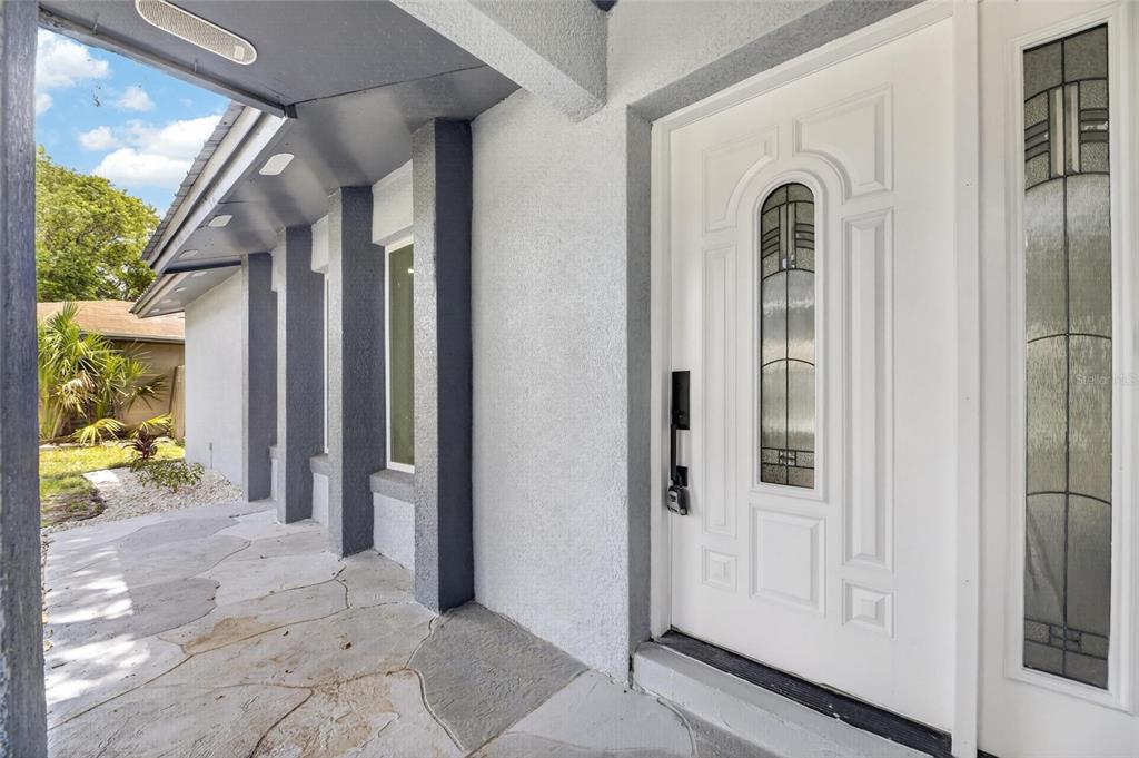 A white front door with glass inserts sits on a covered porch with stone flooring — 3624 COPPERTREE CIRCLE, BRANDON, FL