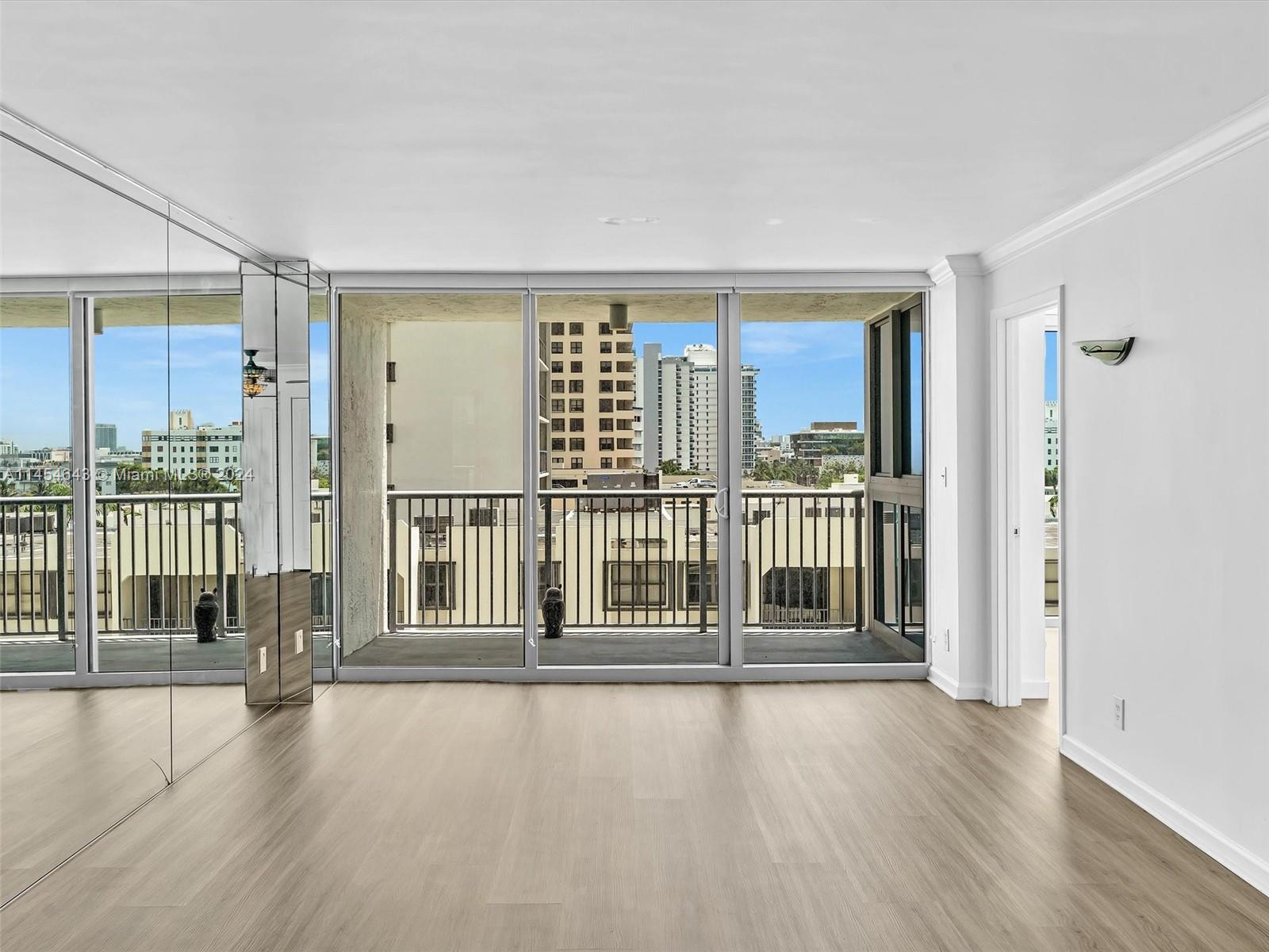 An empty room with light wood floors, mirrored walls, and a balcony overlooking city buildings — 2655 Collins Ave # 706, Miami Beach FL 33140, MIAMI BEACH, FL