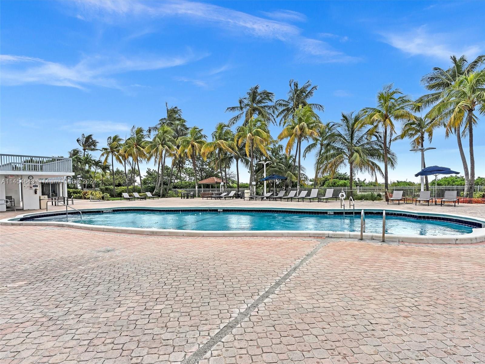 A swimming pool with lounge chairs and palm trees under a blue sky — 2655 Collins Ave # 706, Miami Beach FL 33140, MIAMI BEACH, FL