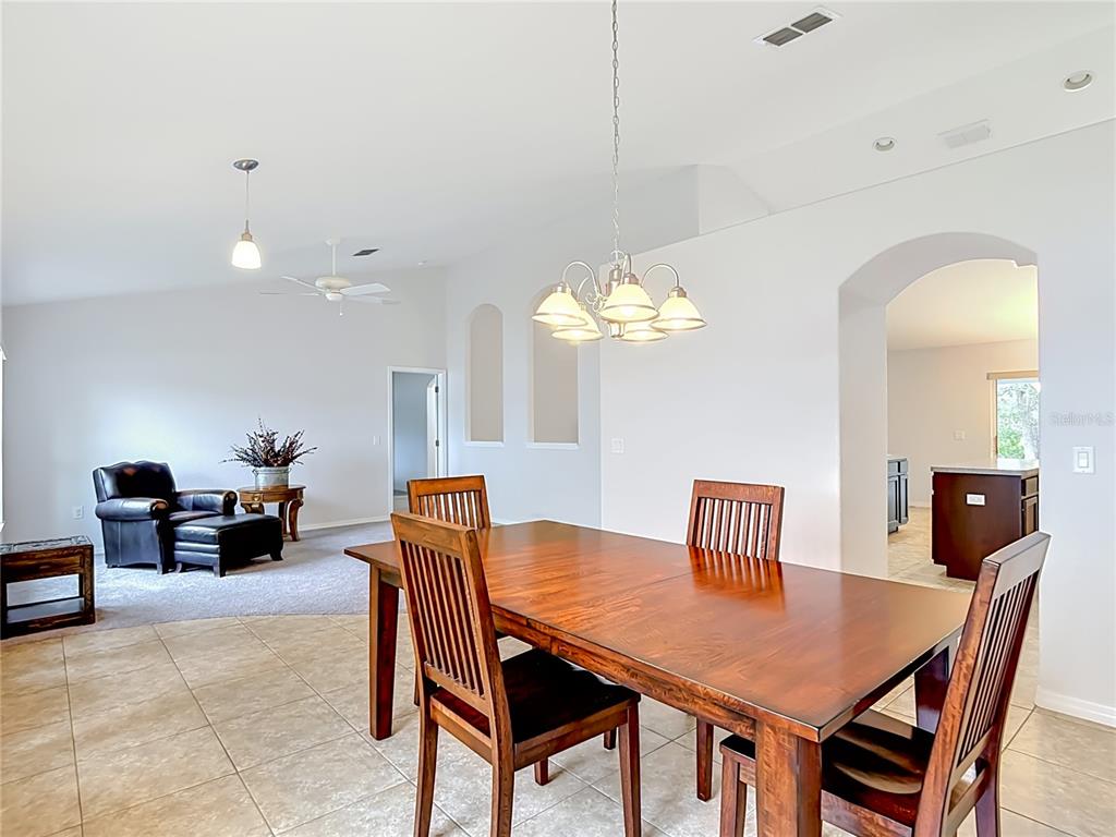 A dining area with a wooden table and chairs sits adjacent to a carpeted living space — 3490 DOW LANE, SPRING HILL, FL