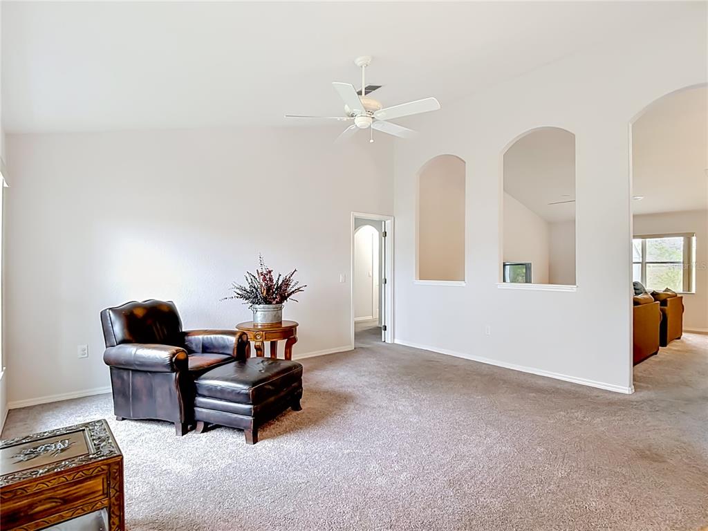 A living room features a leather armchair, carpeted flooring, and two arched wall cutouts — 3490 DOW LANE, SPRING HILL, FL
