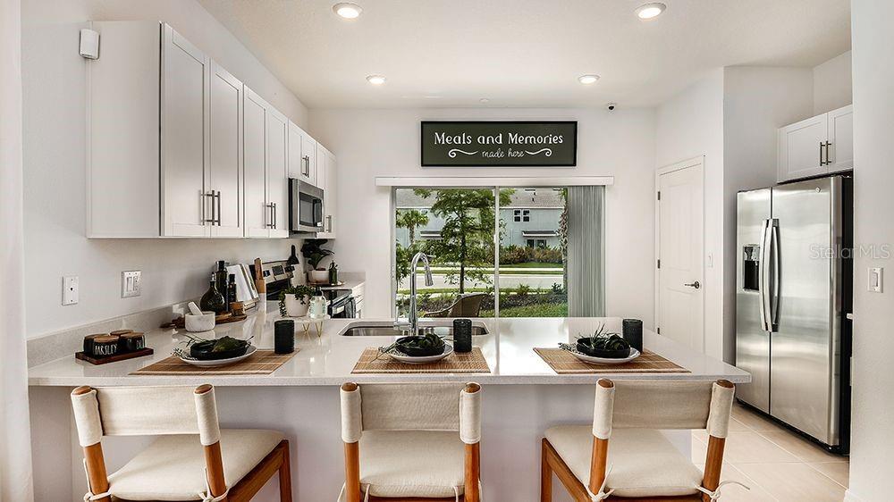 A modern kitchen features white cabinetry, a quartz island with bar seating, and sliding doors — 10633 ORBIT TERRACE, SARASOTA, FL