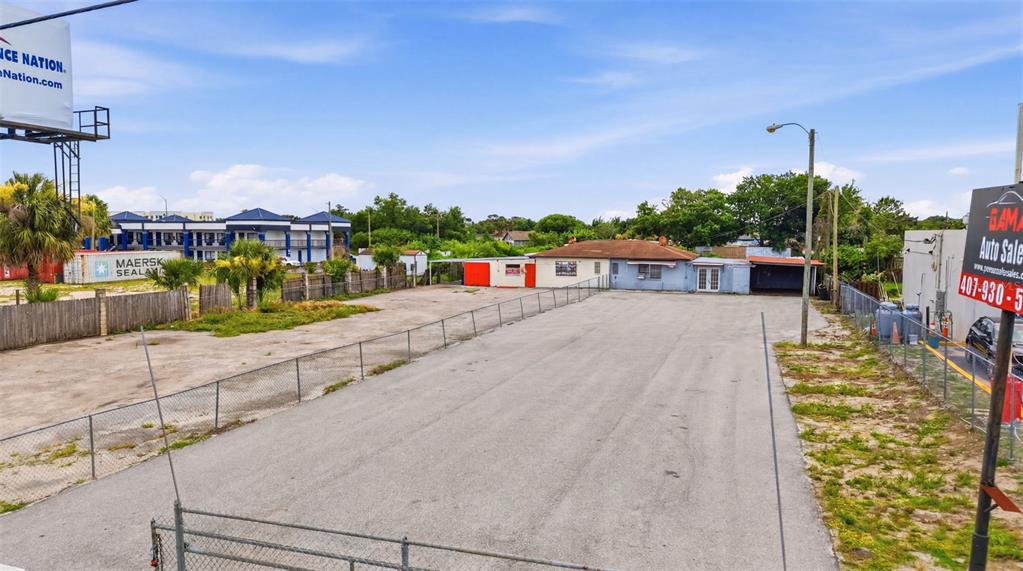An aerial view shows a fenced gravel lot with a small building and storage containers — 8710 E COLONIAL DRIVE, ORLANDO, FL