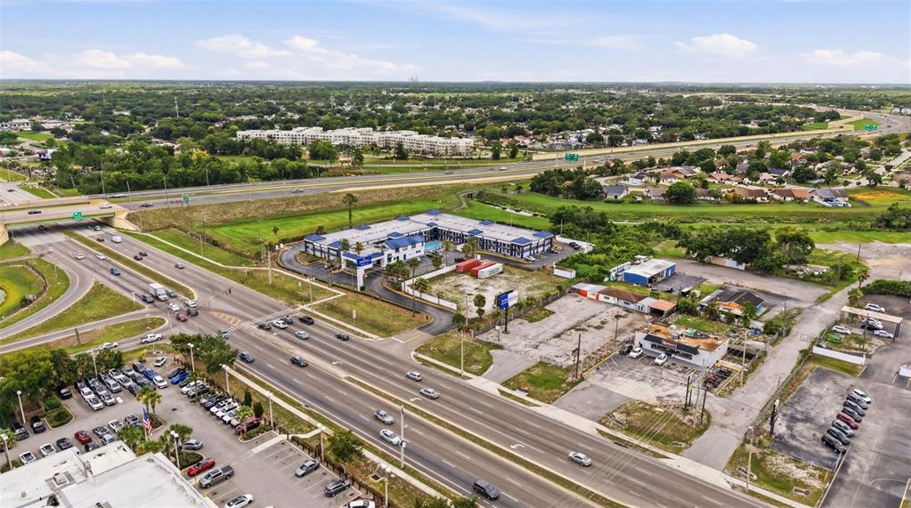 An aerial view shows a hotel with a pool near a highway and commercial buildings — 8710 E COLONIAL DRIVE, ORLANDO, FL
