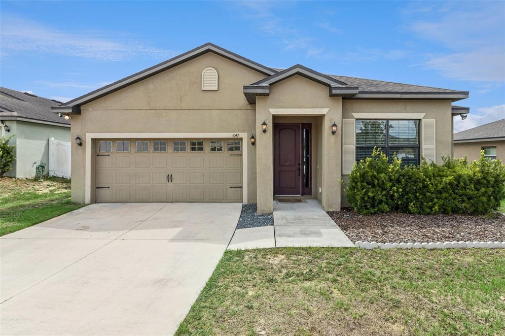 A single-story house with a tan stucco exterior, a two-car garage, and a front entrance — 647 CHICAGO WAY, DUNDEE, FL