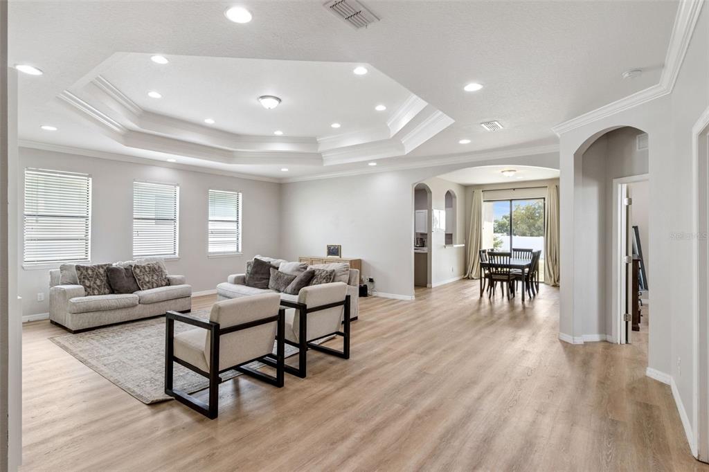A spacious living room with a tray ceiling, light wood flooring, and an adjacent dining area — 647 CHICAGO WAY, DUNDEE, FL