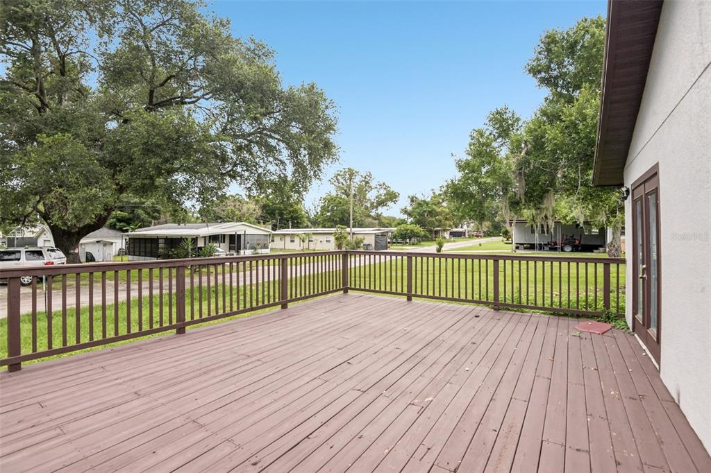 A wooden deck with a railing overlooks a grassy yard and neighboring houses — 37732 CECIL LANE, ZEPHYRHILLS, FL