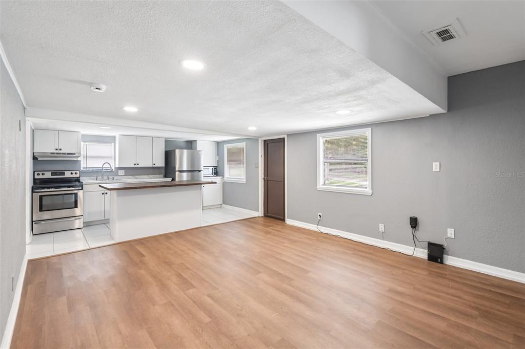 A kitchen with white cabinets and stainless steel appliances opens into a living area — 37732 CECIL LANE, ZEPHYRHILLS, FL