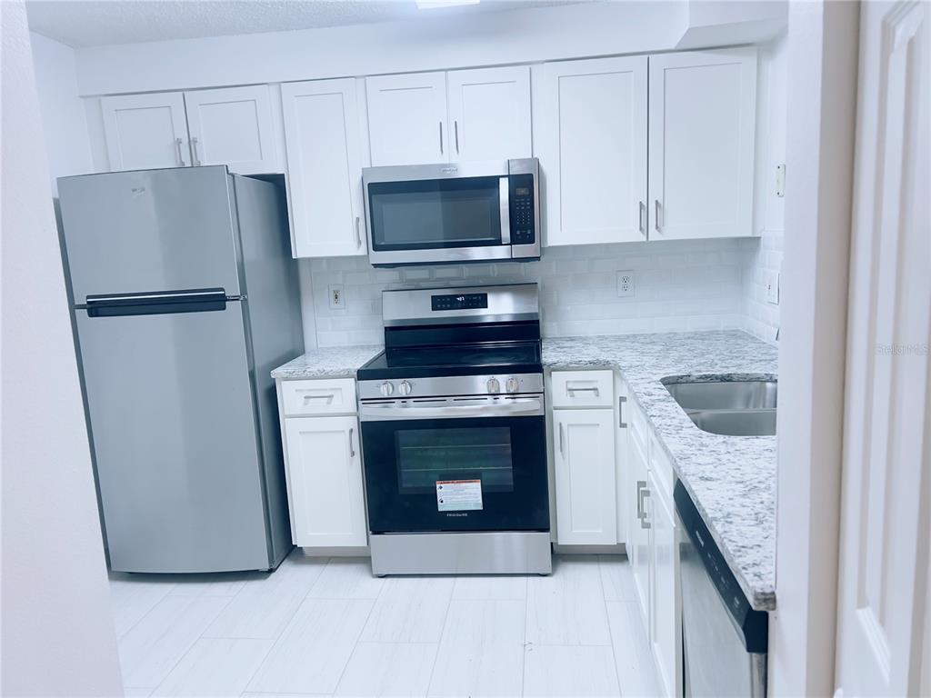 A bright, empty living room features white tile flooring, a chandelier, and glass patio doors — 3508 WINDY WALK WAY UNIT 6101, ORLANDO, FL