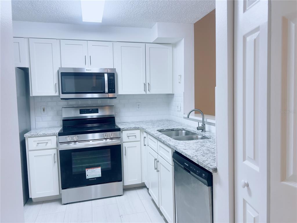 A kitchen features white cabinets, granite countertops, and stainless steel appliances — 3508 WINDY WALK WAY UNIT 6101, ORLANDO, FL