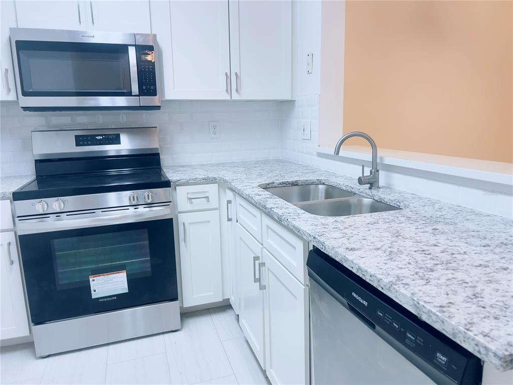 A kitchen features white cabinets, stainless steel appliances, and granite countertops with a subway tile backsplash — 3508 WINDY WALK WAY UNIT 6101, ORLANDO, FL