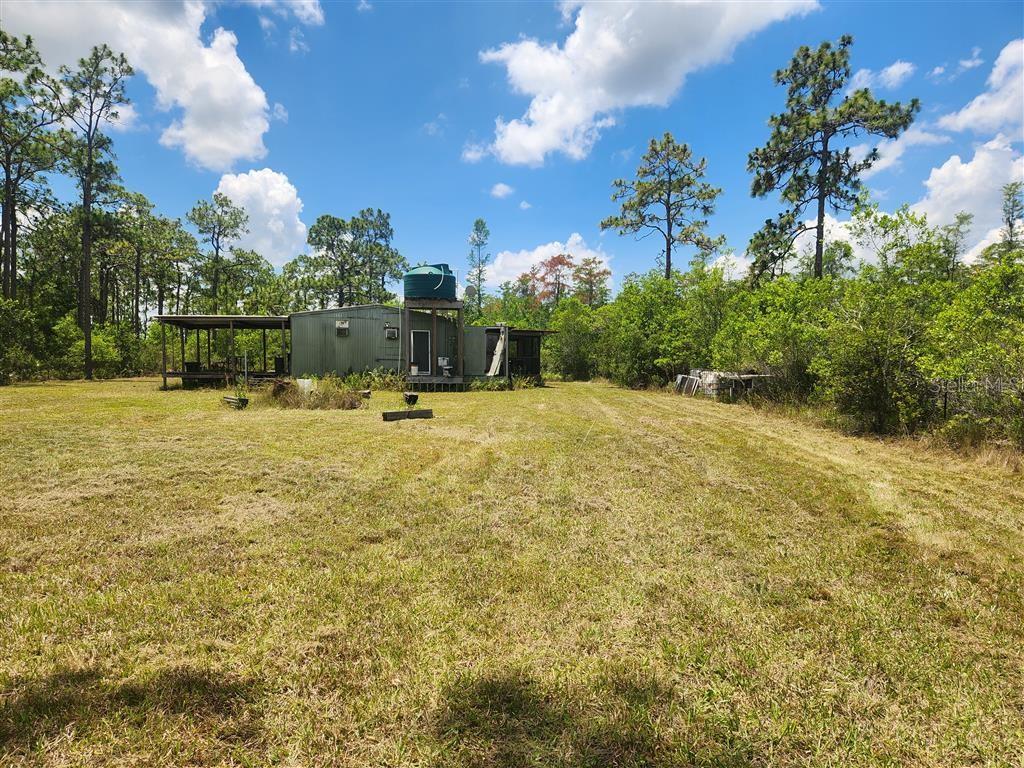 A small, green metal structure with a water tank sits in a grassy field — HOLOPAW GROVES ROAD, ST CLOUD, FL
