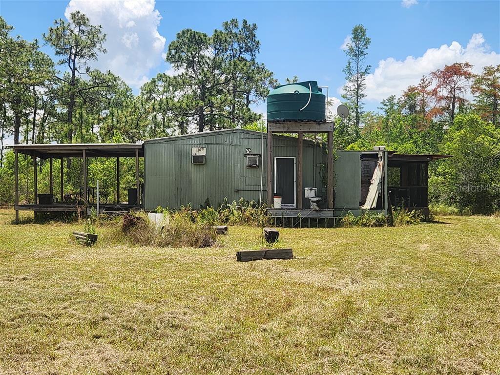 An exterior view of a weathered mobile home with a large green water tank — HOLOPAW GROVES ROAD, ST CLOUD, FL