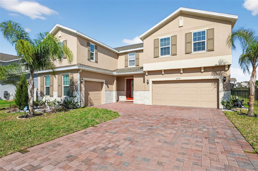 A two-story suburban house with a tan stucco exterior, stone accents, and a brick driveway — 6070 SIERRA CROWN STREET, MOUNT DORA, FL