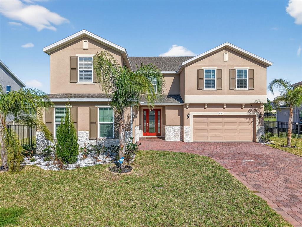A two-story suburban house with a tan stucco exterior, brick driveway, and red front door — 6070 SIERRA CROWN STREET, MOUNT DORA, FL