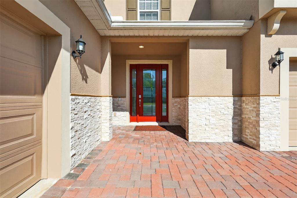 A red front door is centered between two garage doors on a paved entryway — 6070 SIERRA CROWN STREET, MOUNT DORA, FL