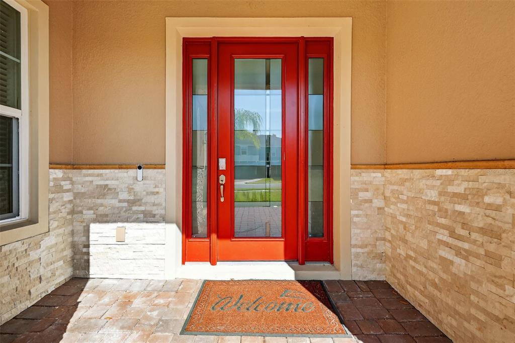 A bright red front door with glass panels sits between stone-clad walls on a porch — 6070 SIERRA CROWN STREET, MOUNT DORA, FL