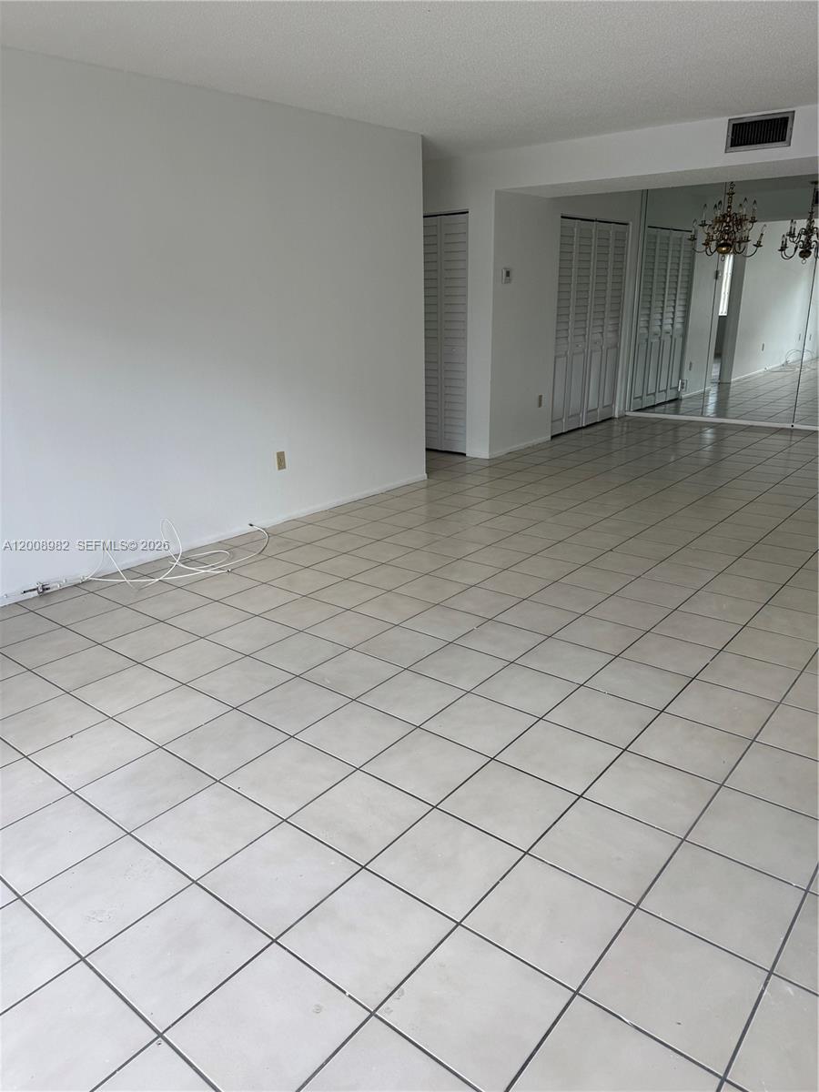 An empty room features light-colored floor tiles, white walls, and a mirrored wall section — 7747 SW 86th St # 105, Miami FL 33143, MIAMI, FL