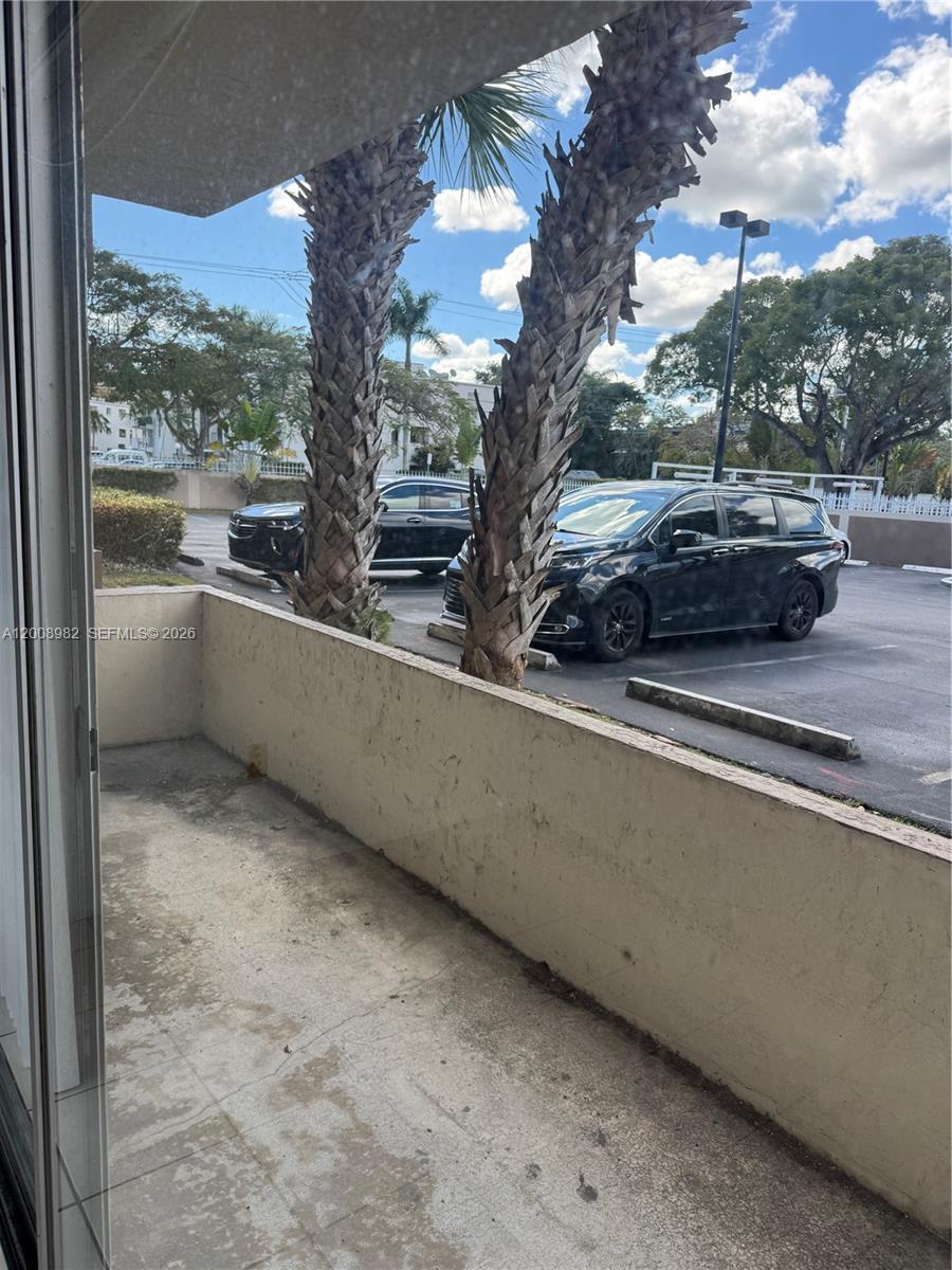A concrete balcony overlooks a parking lot with two palm trees and two parked cars — 7747 SW 86th St # 105, Miami FL 33143, MIAMI, FL