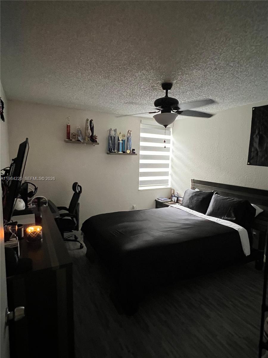 A bedroom features a dark bed, a desk with a computer, and two wall-mounted shelves — 1900 W 68th St # F104, Hialeah FL 33014, HIALEAH, FL