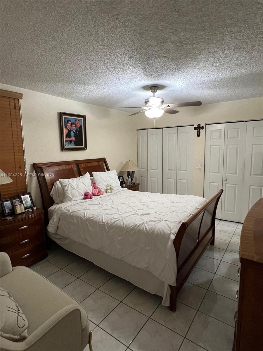 A bedroom features a wooden bed frame, white bedding, tiled floors, and white closet doors — 1900 W 68th St # F104, Hialeah FL 33014, HIALEAH, FL