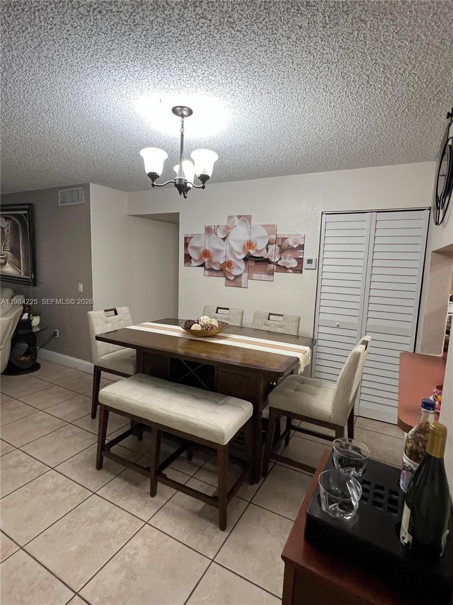 A dining room features a wooden table with chairs and a bench on tiled floors — 1900 W 68th St # F104, Hialeah FL 33014, HIALEAH, FL