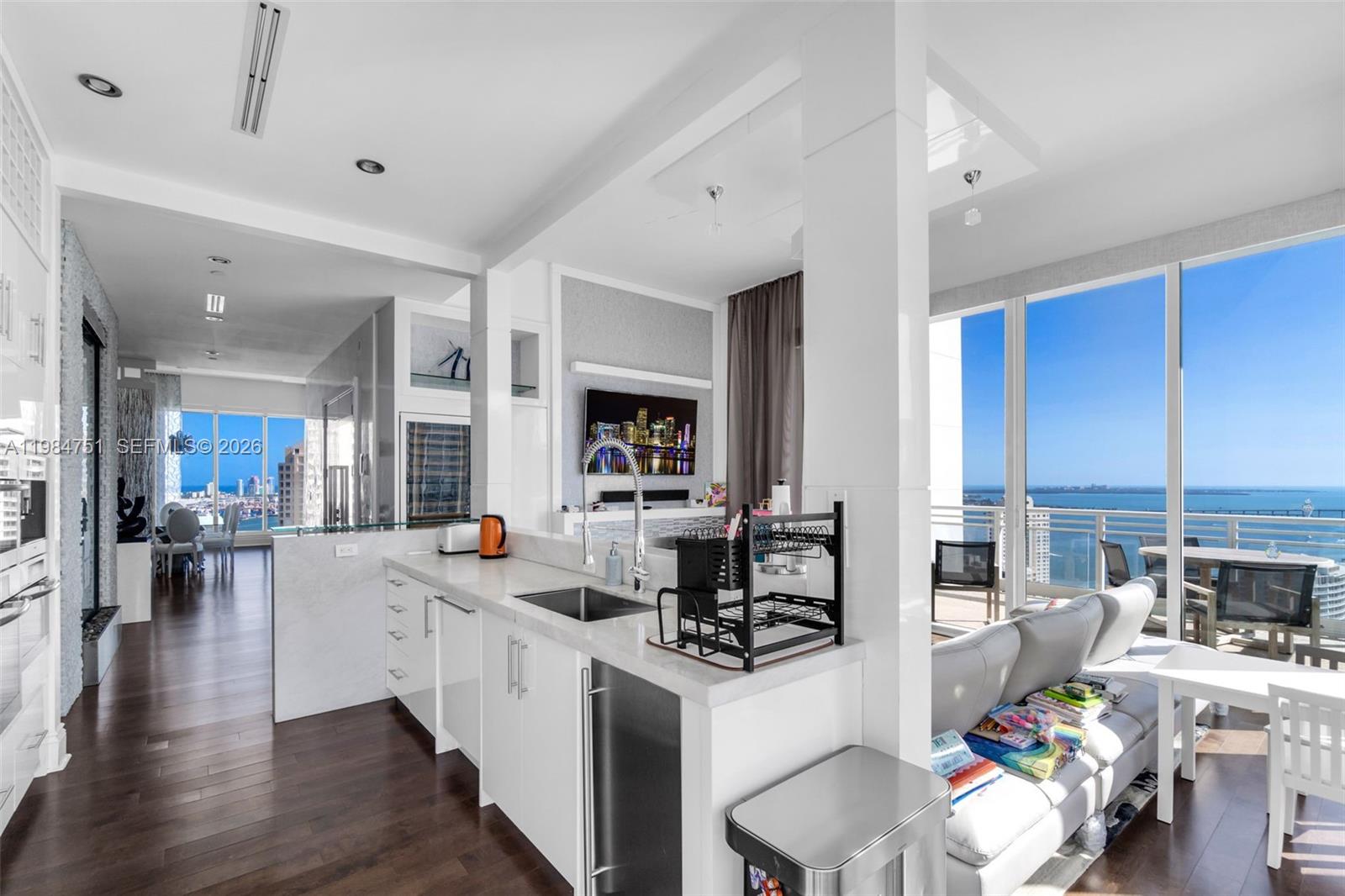 A modern kitchen with white cabinetry and marble countertops overlooks a living area and balcony — 900 Brickell Key Blvd # 2904, Miami FL 33131, MIAMI, FL