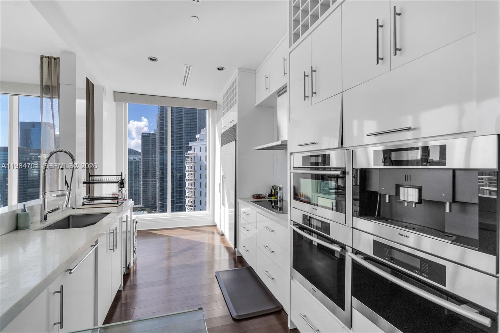 A modern kitchen features white cabinetry, stainless steel appliances, and a window with city views — 900 Brickell Key Blvd # 2904, Miami FL 33131, MIAMI, FL