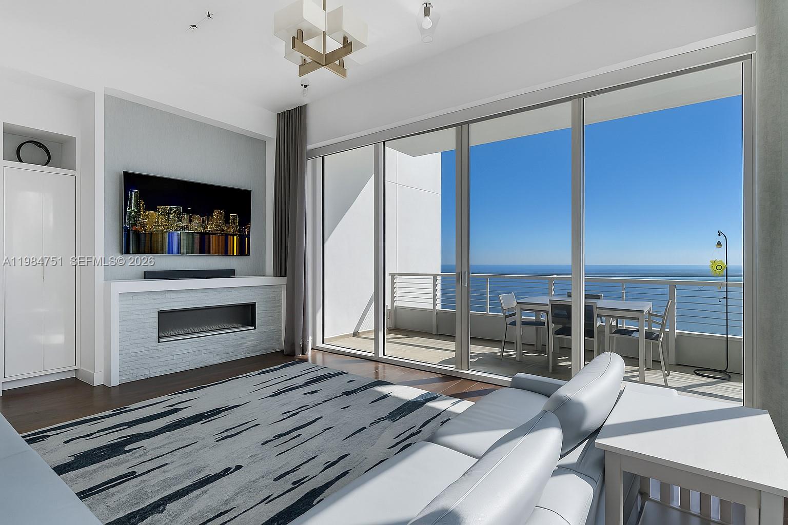 A modern living room features a fireplace, wall-mounted television, and floor-to-ceiling windows overlooking the ocean — 900 Brickell Key Blvd # 2904, Miami FL 33131, MIAMI, FL