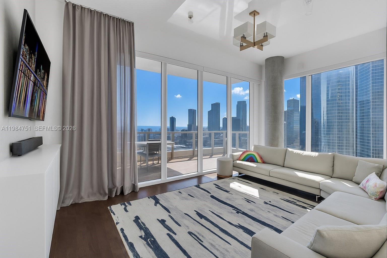 A modern living room features a white sectional sofa, patterned rug, and floor-to-ceiling windows — 900 Brickell Key Blvd # 2904, Miami FL 33131, MIAMI, FL