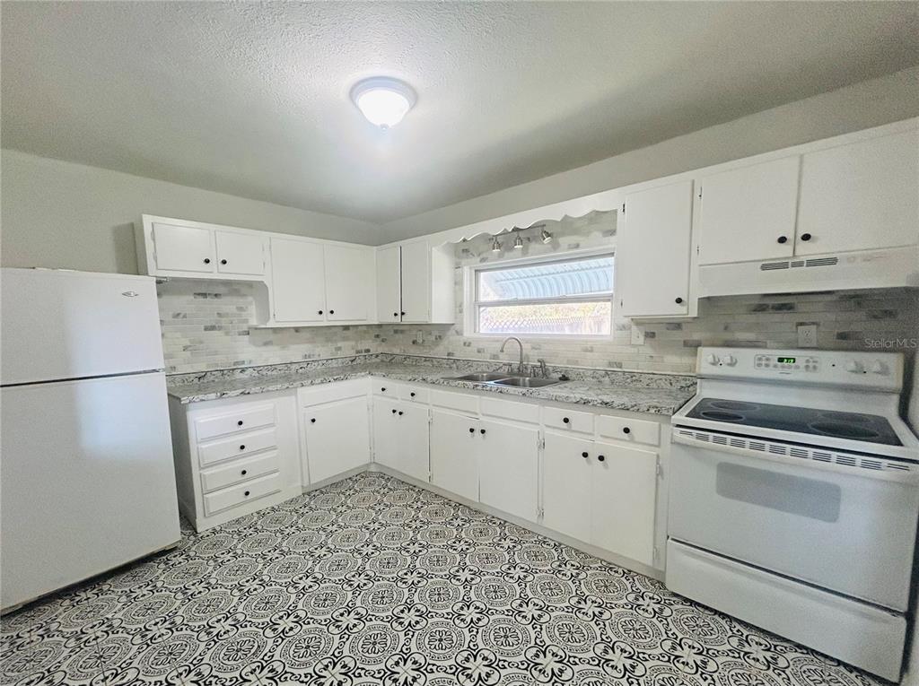 A kitchen features white cabinets, granite countertops, a tiled backsplash, and patterned floor tiles — 3824 AUTUMN PALM DRIVE, ZEPHYRHILLS, FL