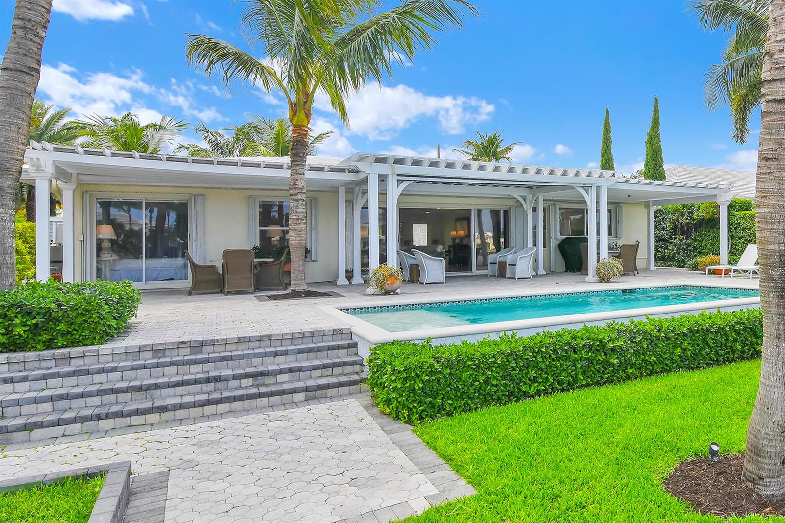 A backyard features a swimming pool, a covered patio, and a paved stone walkway — 3211 Karen Drive, Delray Beach FL 33483, DELRAY BEACH, FL