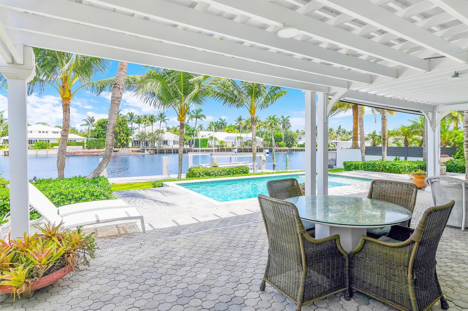 A covered patio features a dining set and lounge chairs overlooking a pool and canal — 3211 Karen Drive, Delray Beach FL 33483, DELRAY BEACH, FL