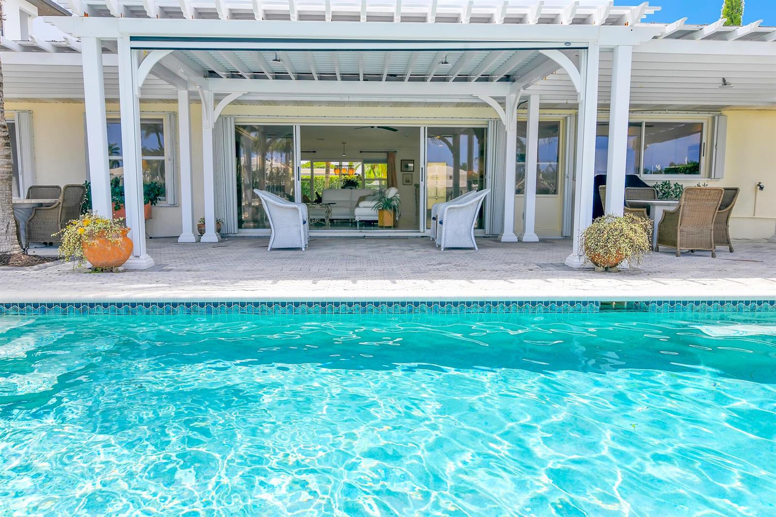 A swimming pool sits in front of a covered patio with white columns and furniture — 3211 Karen Drive, Delray Beach FL 33483, DELRAY BEACH, FL