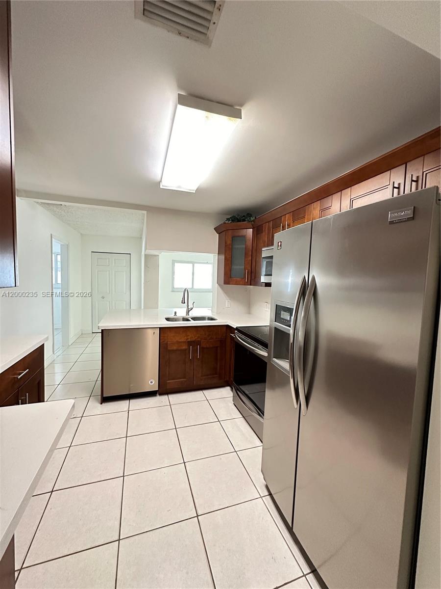 A kitchen features stainless steel appliances, dark wood cabinetry, and white countertops over tile flooring — 17335 SW 108th Ct, Miami FL 33157, MIAMI, FL