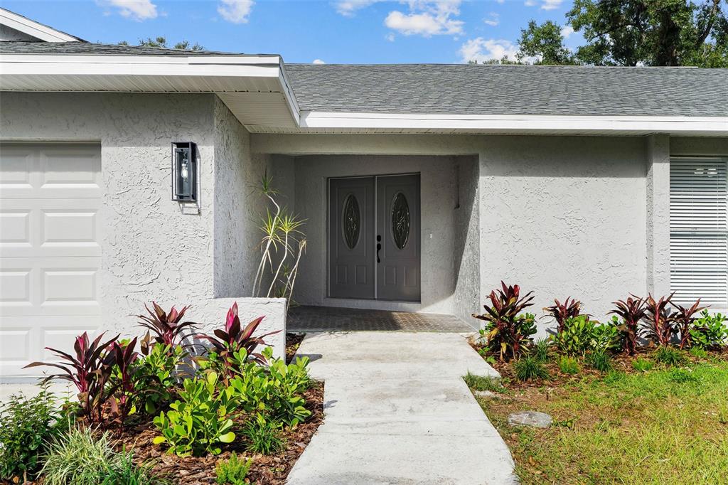 A concrete walkway leads to the gray double front doors of a single-story house — 1106 HUMMINGBIRD LANE, BRANDON, FL