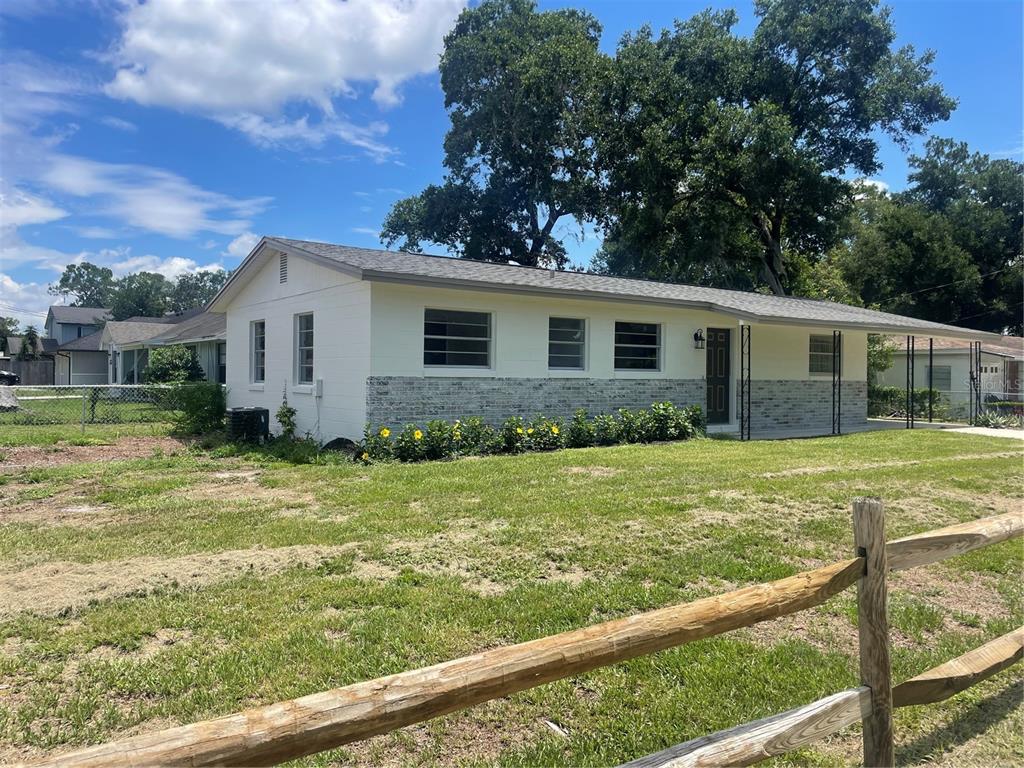 A single-story house with white siding, stone accents, and a carport sits on a grassy lot — 611 ORANGE AVENUE, LONGWOOD, FL