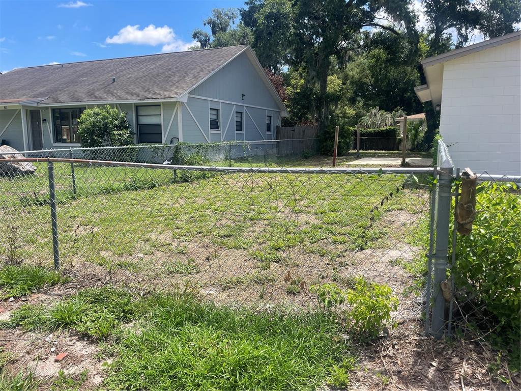 A chain-link fence encloses a grassy yard between two residential buildings — 611 ORANGE AVENUE, LONGWOOD, FL