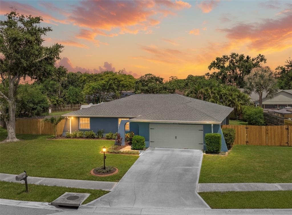A blue single-story house with a two-car garage and a concrete driveway at sunset — 6553 SAMOA DRIVE, SARASOTA, FL
