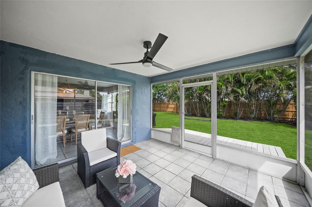 A screened-in patio with tile flooring, wicker furniture, and a view of a grassy backyard — 6553 SAMOA DRIVE, SARASOTA, FL