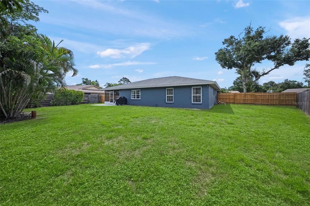 The backyard of a single-story house features a grassy lawn and a wooden fence — 6553 SAMOA DRIVE, SARASOTA, FL
