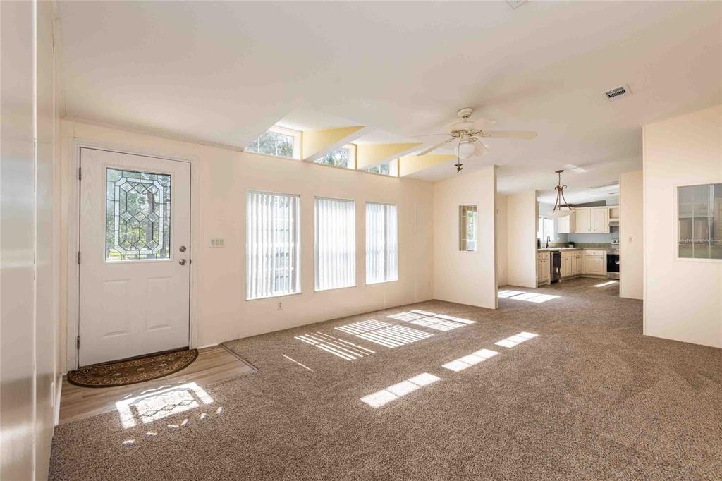 A carpeted living room features a white front door, large windows, and a ceiling fan — 14221 HURRICANE DRIVE, WEEKI WACHEE, FL