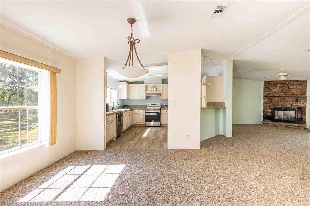 A carpeted living area opens into a kitchen with light-colored cabinets and a stone fireplace — 14221 HURRICANE DRIVE, WEEKI WACHEE, FL