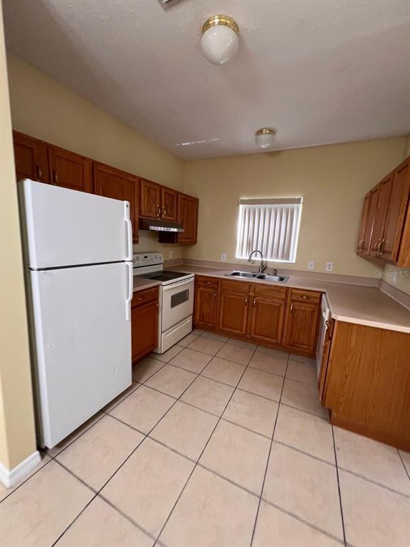 A kitchen features wood cabinets, white appliances, tile flooring, and a double sink — 201 WATTS LANE UNIT A, KISSIMMEE, FL