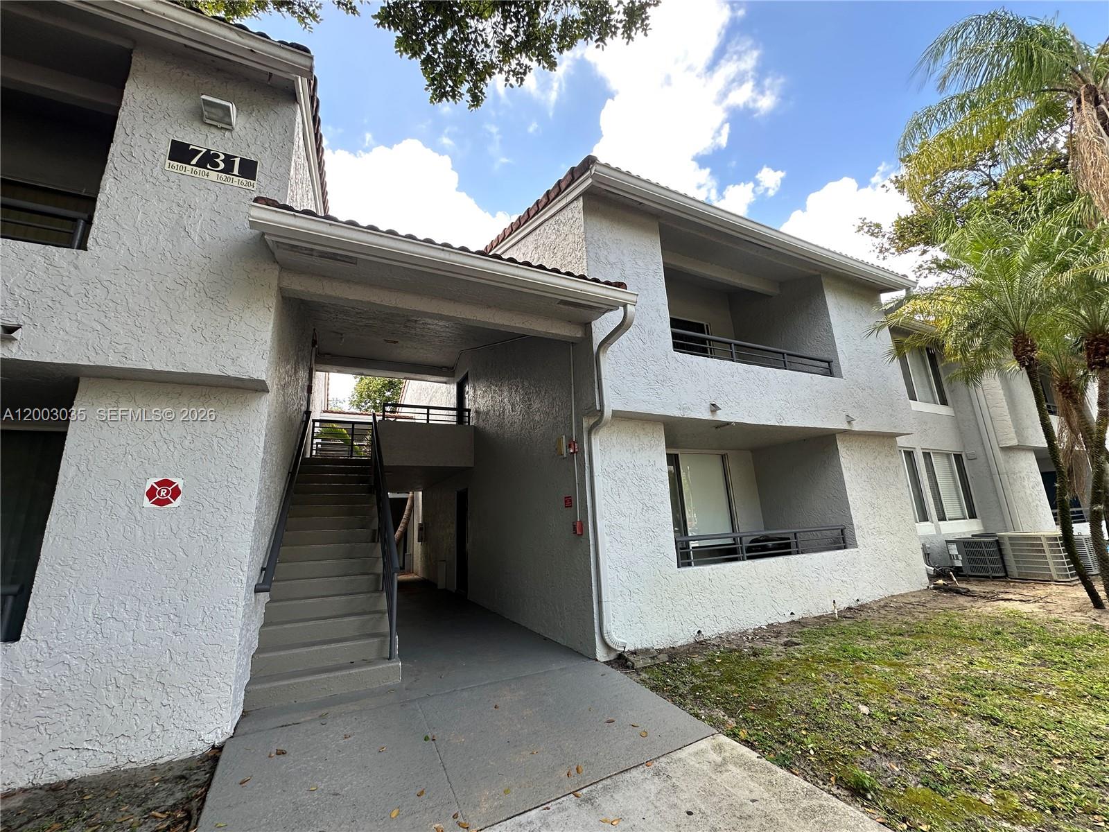 A two-story apartment building exterior features a concrete staircase leading to an upper-level walkway — 731 Lyons Rd # 16203, Coconut Creek FL 33063, COCONUT CREEK, FL