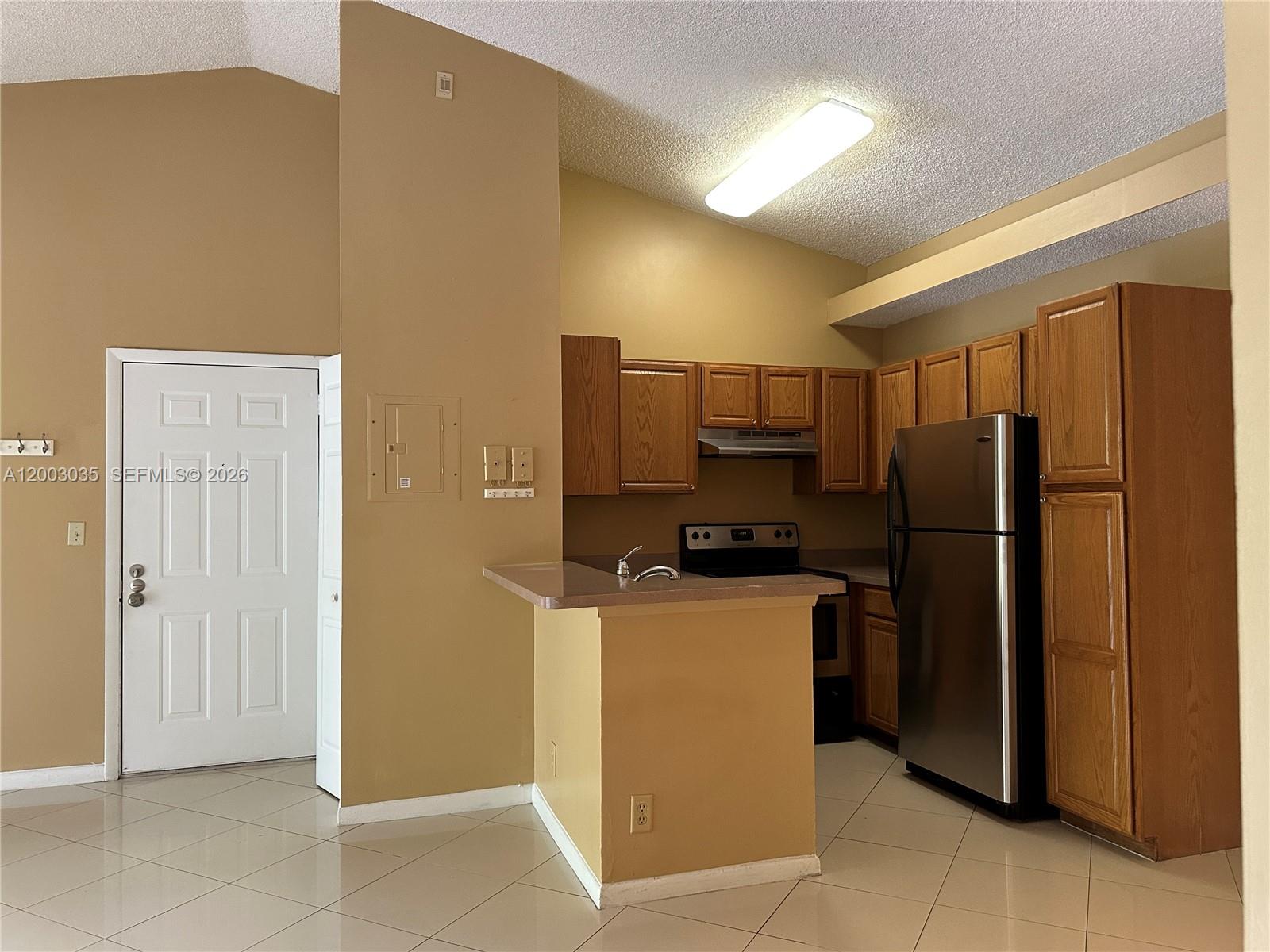 A kitchen features light-colored tile floors, tan walls, oak cabinets, and stainless steel appliances — 731 Lyons Rd # 16203, Coconut Creek FL 33063, COCONUT CREEK, FL