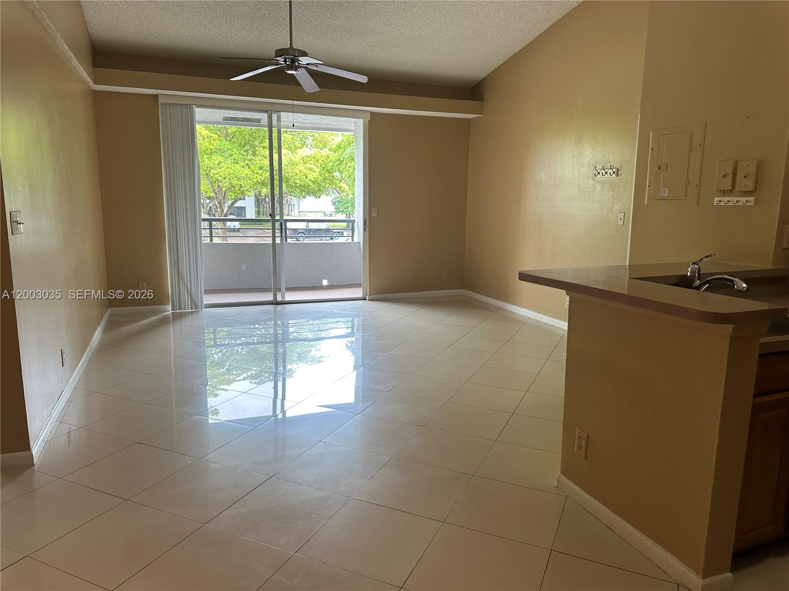 An empty living area features light-colored tile flooring, a ceiling fan, and a sliding glass door — 731 Lyons Rd # 16203, Coconut Creek FL 33063, COCONUT CREEK, FL