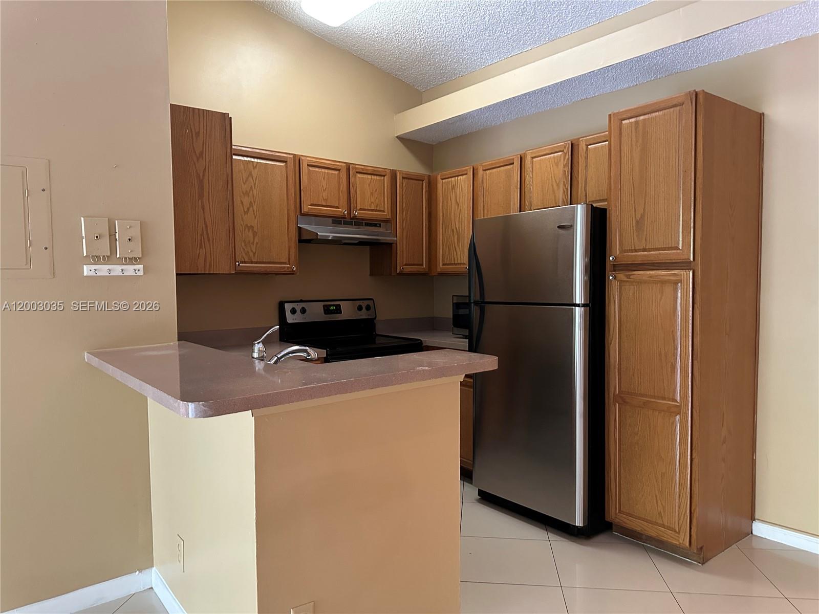 A kitchen features oak cabinets, a stainless steel refrigerator, and a peninsula with a sink — 731 Lyons Rd # 16203, Coconut Creek FL 33063, COCONUT CREEK, FL