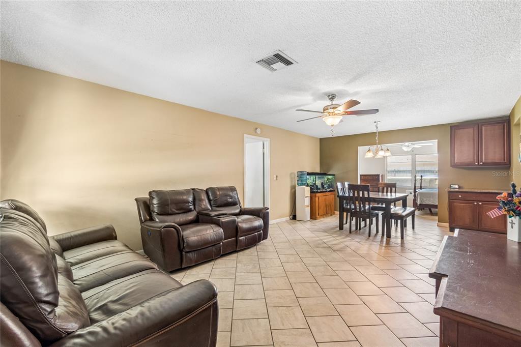 A living room with tile flooring, brown leather furniture, and an adjacent dining area — 9473 BAYSIDE COURT, SPRING HILL, FL